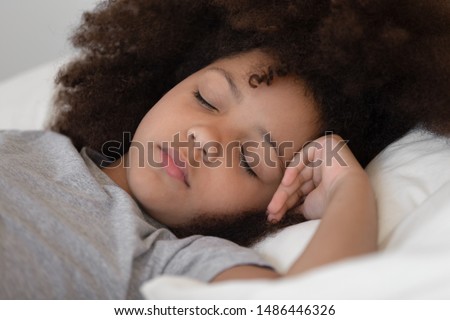 Close up cropped image mixed race cute peaceful child girl napping in bed. African american adorable preschool kid sleeping alone on soft pillow, resting at night or daydreaming in bedroom at home.