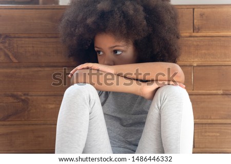 Close up cropped cute offended little african american girl sitting on floor, feeling lonely, suffering from misunderstanding, quarrel with parents or friends. Sad orphan being abused or bullied. Royalty-Free Stock Photo #1486446332