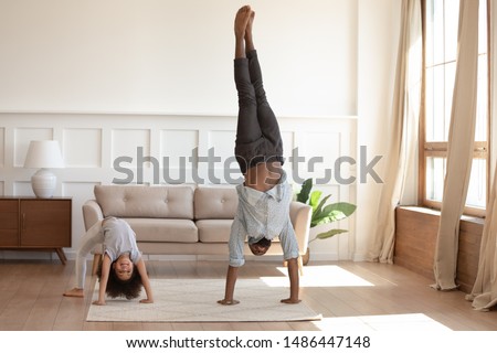 Active happy african american girl doing bridge exercise, strong father staying on hands. Smiling black family doing morning exercises together in living room at home. Daily healthy habit concept.