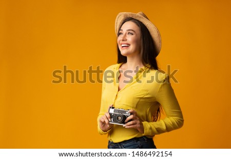 Travel Photo. Woman Holding Retro Camera Sightseeing And Taking Pictures On Vacation Over Yellow Studio Background. Empty Space