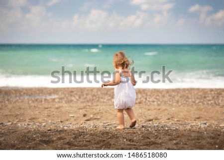 Cute oneyear babygirl, walking on the ocean beach. Backside view