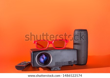 Home Theater Set: projector with tv-remote, 3d glasses, wireless speaker. Orange isolated background