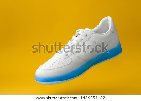 trendy white sneakers with blue sole  isolated on yellow background 