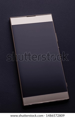 Gold colored smartphone with blank screen closeup flat on black background, top view