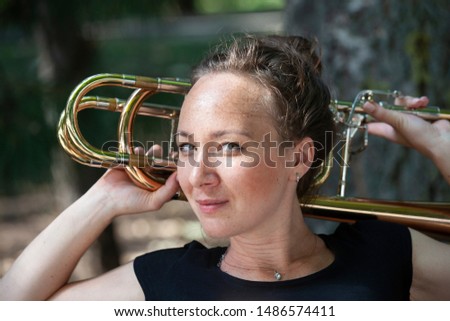 Girl learning to play trombone. Portrait of a girl on a background of a city park park. Portrait. Close-up.