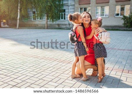Happy mother meeting her kids daughters after classes outdoors primary school. Family hugging. Back to school