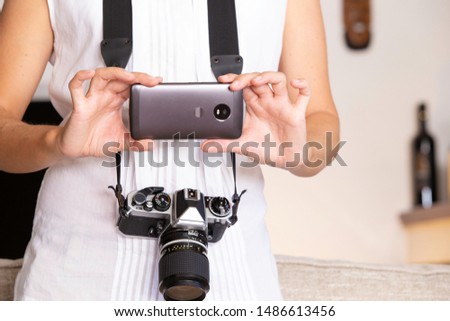 Contrast between old and modern times: a young woman with a vintage camera around her neck fiddles with her smartphone