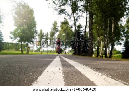 Sportswoman in uniform and helmet riding on the bike path on the background of green trees. Selective focus on the pavement