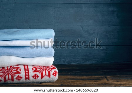 Pile stack folded of knitted winter clothes on wooden background, sweaters, knitwear, copy space for text.