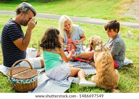 Family in the park for a picnic in their summer holiday. Father takes a picture with his vintage photo camera. Focus on dad's face. Travel, parenthood, summer and love concept.