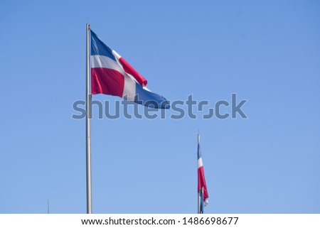 Two Flag of Dominican Republic (DR) waving in the wind with blue sky on background