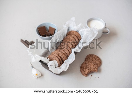 Homemade Crinkles Fudgy milk chocolate cookies in baking tin and white parchment paper with a cup of milk on light gray background