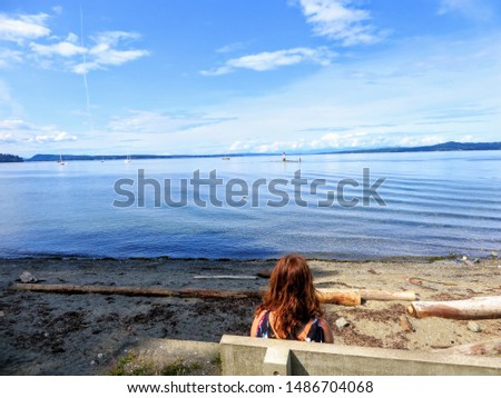 A young woman deep in thought sitting on a bench that looks outward to the ocean full of boats  on a beautiful sunny summer day in Chemainus, Vancouver island, British Columbia, Canada.