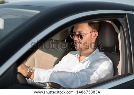 Happy driver in a white shirt and sun glasses drives his luxary car. Concept of success.