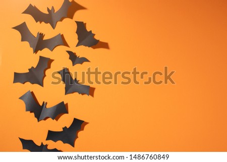 Halloween picture of black bats flying up on blank orange background.