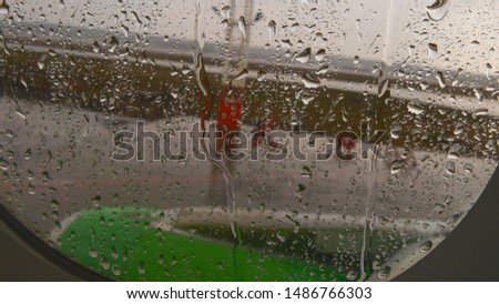 Flying a plane in the rain. Raindrops on airplane window. Drops of water on the glass with a blurred background airplane wings with green engine and airport runway.Travel, tourism and vacation concept