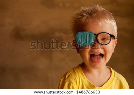 Portrait of funny child in new glasses with patch for correcting squint 
Ortopad Boys Eye Patches nozzle for glasses for treatment of strabismus (lazy eye) Royalty-Free Stock Photo #1486766630