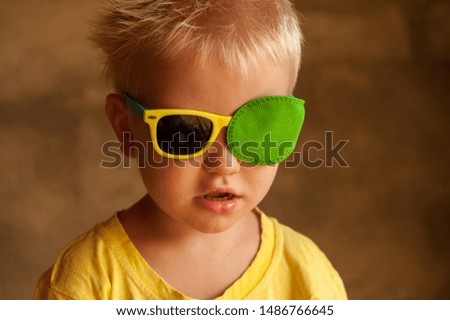 Portrait of funny child in new glasses with patch for correcting squint 
Ortopad Boys Eye Patches nozzle for glasses for treatment of strabismus (lazy eye)