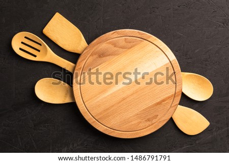 Wooden kitchen utensils and empty round tray for cooking on dark background,copy space