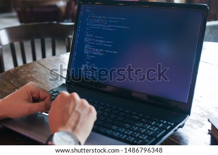 Neat hands lie on the keyboard of a laptop standing on an old desk in the library. On the monitor site code. Website development, coding. Close-up, blurred background.