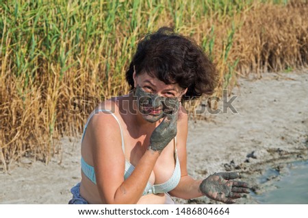 Elderly woman takes mud mask for problem areas of body in natural conditions of salt lake