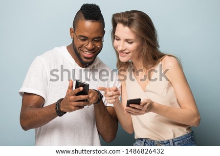 Smiling african American man talk show news on smartphone to beautiful Caucasian woman, happy multiracial diverse young people isolated on blue studio background using cellphones together Royalty-Free Stock Photo #1486826432