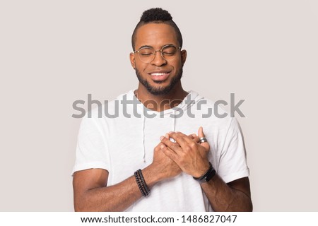 Grateful african American man in glasses hold hand close to heart at chest show love and appreciation, thankful black man stand isolated on grey studio background feel pleased and sincere Royalty-Free Stock Photo #1486827047