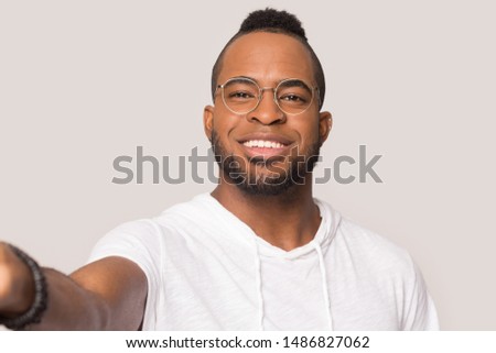 Smiling african American millennial male in glasses isolated on grey studio background make self-portrait picture, happy black man in eyewear look at camera hold gadget taking selfie