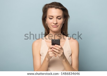 Smiling beautiful young woman isolated on blue studio background hold smartphone texting or messaging, happy millennial female using cellphone surfing browsing internet or shopping online