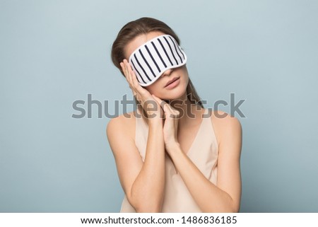 Tired woman wearing sleeping mask isolated on blue studio background relax fall asleep on hands, exhausted calm female in cozy homewear rest sleep standing, dream seeing sweet dreams