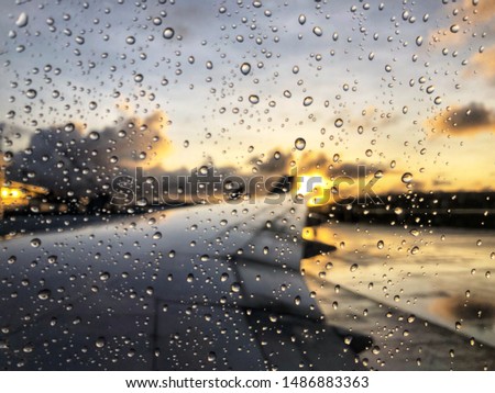 Raindrops on airplane window with blurred background of morning sunrise and sky clouds. Guam airport USA.