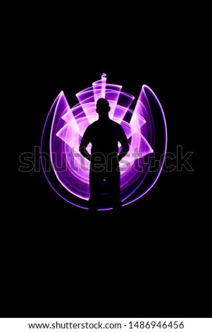 Silhouette of a man standing from the front. Curved abstract shapes made of violet light saber in background. Lightpainting session in long exposure at night.