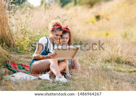 Young attractive mother teaches daughter painting in summer park. Outdoors activity for school age children concept