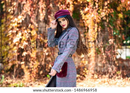 Young beautiful girl with very long hair wearing winter coat and cap in autumn leaves background. Lifestyle and fashion concept.