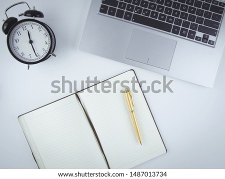 On the desktop is a computer, an alarm clock and a notebook with a pen. Flat design lay workplace desk with laptop, blank notebook, golden pen, alarm clock, with copy space background.