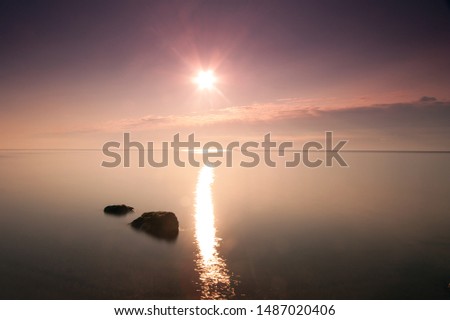 Seascape after sunrise with  reflection of the sun track and stones in the foreground