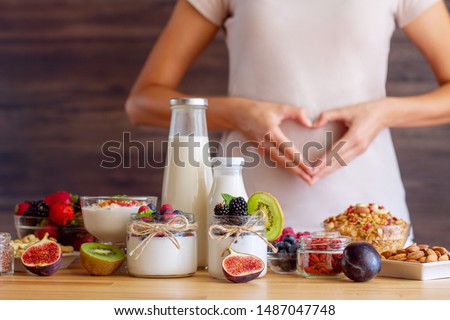 Female make shape of heart with her hands. Light summer breakfast with organic yogurts, fruits, berries and nuts. Nutrition that promotes good digestion and functioning of gastrointestinal tract. Royalty-Free Stock Photo #1487047748