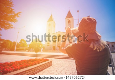 MEDUGORJE, BOSNIA AND HERZEGOVINA - JULY 12, 2019: Virgin Mary statue and the parish church of St. James, the shrine of Our Lady of Medugorje. Young woman standing in front turned from behind