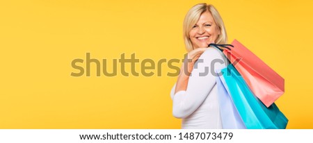 Buyer. Consumer. Sale. Customer. Online Shopping. Happy laughing blonde senior woman with colorful paper shopping bags is posing and has a fun after good visit of mall. Banner photo