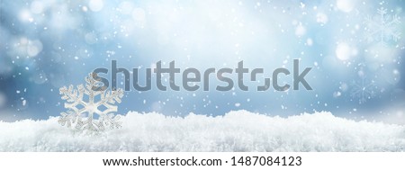 Festive winter snow background with snowdrifts, silver decorative snowflake with beautiful light and snow flakes on blue sky, banner format, copy space.