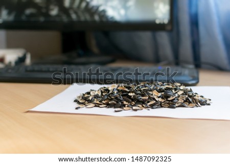 a pile of sunflower seed skins on a clean sheet of paper lies on the table against the computer screen and keyboard