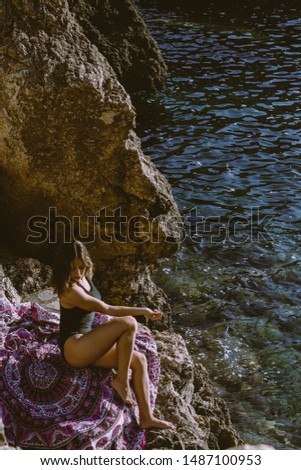 Young woman sunbathing in front of the sea on the rocks. Concept of relaxation and sunbathing holidays. Beauty and personal care on the beach.  Vertical orientation with copyspace.