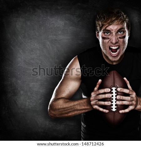 Football player aggressive portrait holding american football on black blackboard background with copy space for text or design. Caucasian male model in his 20s.