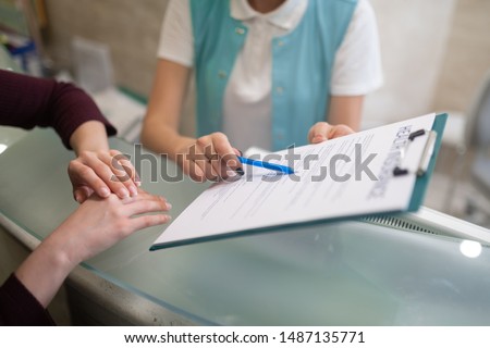 Form to fill. Receptionist of private dentistry showing the form to fill in and sign before examination