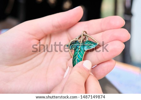 Pendant elven leaf in woman hands. Decoration in the form of a green Shamrock brooch. Trefoil jewelry for women, the symbol of the elven leaf.
