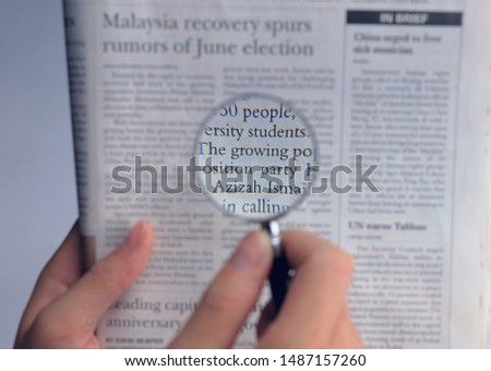 Close up photo of hand holding newspaper and reading with magnifying glass