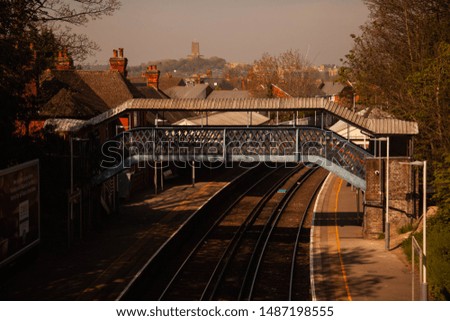 In this picture you can find a bridge over train tracks. The bridge is located in a train station in England. The photo has a  warm/orange and contrasty overall look.