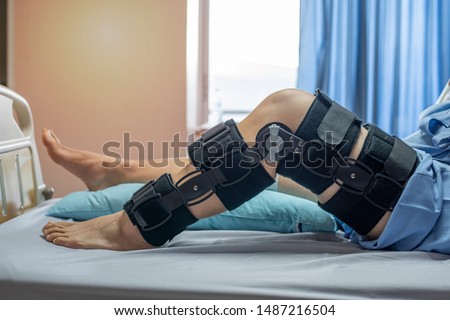 Asian woman patient with bandage compression knee brace support injury on the bed in nursing hospital.healthcare and medical support. Royalty-Free Stock Photo #1487216504