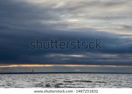 Small yacht on the waves against the background of the gloomy sky. Sun rays through the clouds. Windy, the sea is worried. Sail on the horizon.