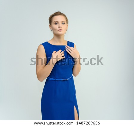 Photo studio portrait of a pretty young woman girl in a beautiful blue dress on a white background. He stands right in front of the camera, explains with emotion.